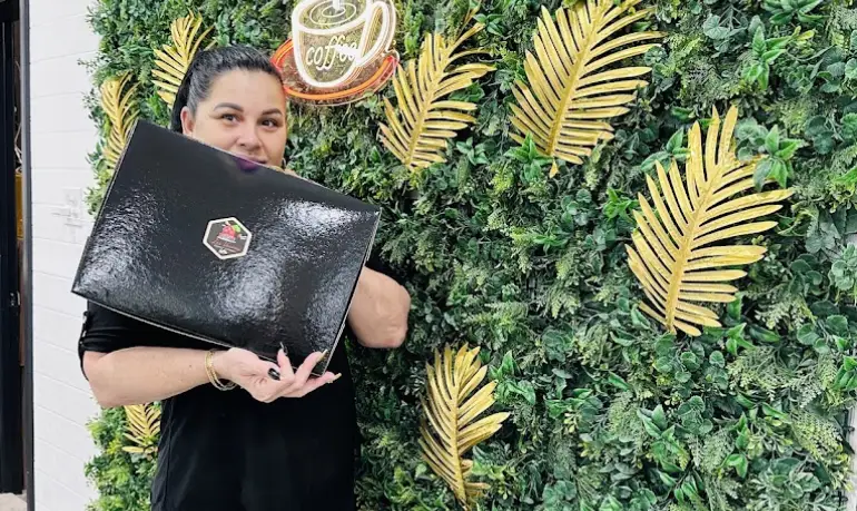 Los Vecinos team member smiling in front of tropical leaf wall with coffee neon sign