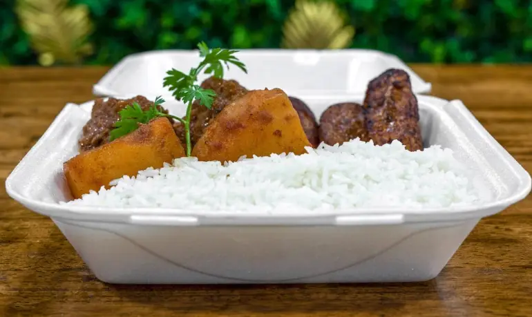 Homestyle Cuban meal with white rice, seasoned potatoes, and meat served in Los Vecinos takeout container